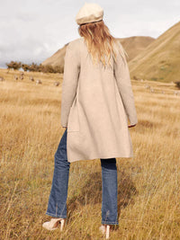 Frau in beigem Mantel und Jeans auf Wiese, Herbstmode, stilvoll, lässig, Outdoor-Look.