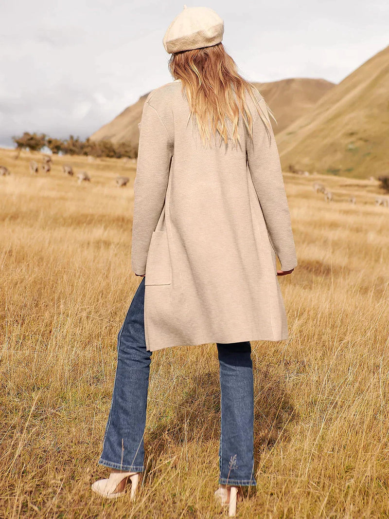 Frau in beigem Mantel und Jeans auf Wiese, Herbstmode, stilvoll, lässig, Outdoor-Look.