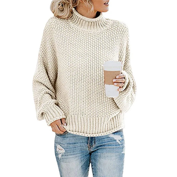 Frau in cremefarbenem Strickpullover mit Kaffeebecher und zerrissenen Jeans.