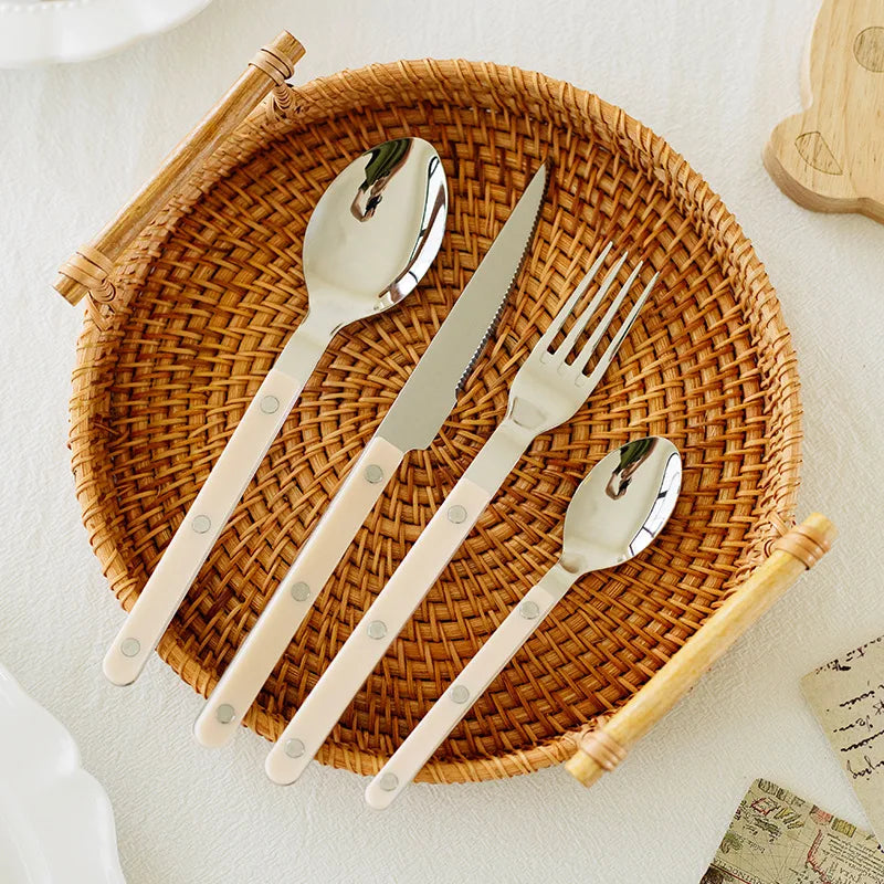 Besteckset aus Edelstahl mit cremefarbenen Griffen auf einem runden, geflochtenen Tablett.