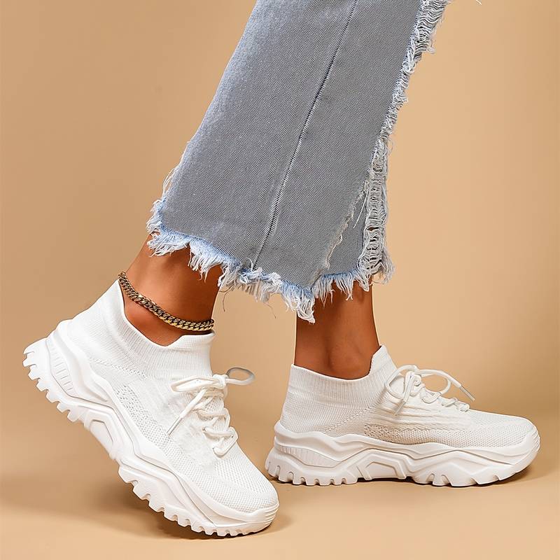 Weiße Damen-Sneaker mit dicker Sohle, gestricktes Material, modisch, bequem, Jeans-Hintergrund.