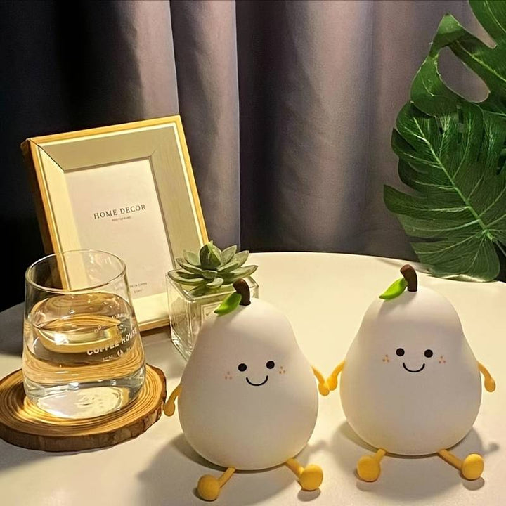 Zwei lächelnde Birnen-Nachtlichter aus Kunststoff auf Tisch, neben Glas und Pflanze.