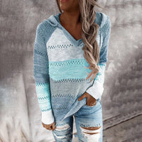 Frau in blauem Strickpullover mit Kapuze und zerrissenen Jeans vor grauem Hintergrund.