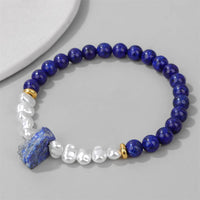 Blaues Lapislazuli-Armband mit weißen Perlen und goldenen Akzenten auf grauem Hintergrund.