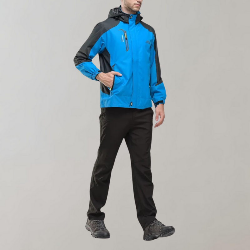 Mann in blauer Outdoor-Jacke mit Kapuze, schwarze Hose, graue Schuhe, sportlich, funktional.