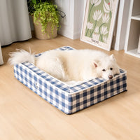 Weißer Hund auf blau-weiß kariertem Hundebett, gemütlich, im Wohnzimmer, Holzboden.