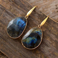 Labradorit-Ohrringe mit goldener Fassung, facettiert, auf Holzoberfläche.