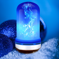 Blaue LED-Lampe mit Flammeneffekt, dekorativ, auf Schnee, neben blauen Kugeln.