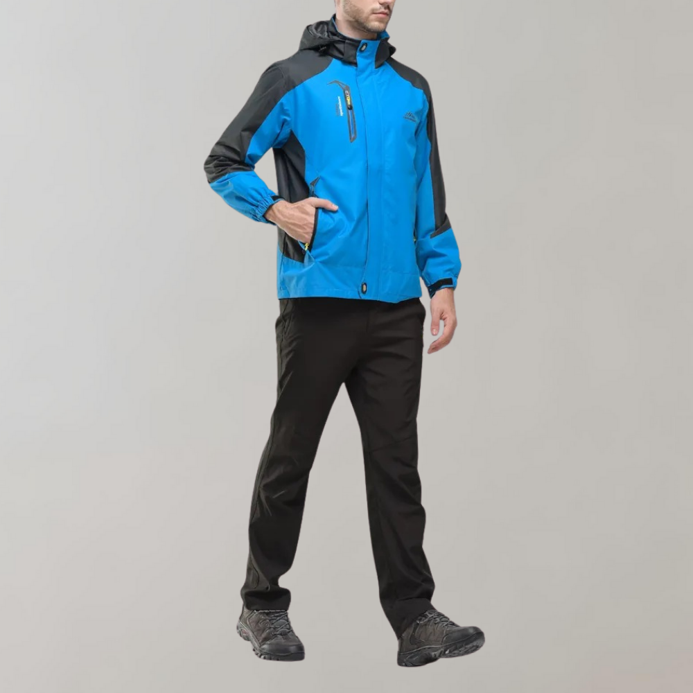 Mann in blauer Outdoor-Jacke mit Kapuze, schwarze Hose, graue Schuhe, sportlich, funktional.