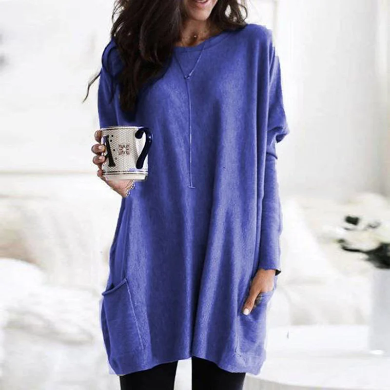Frau in blauem Oversize-Pullover mit Kaffeetasse, gemütliche Wintermode, Wohnzimmer.