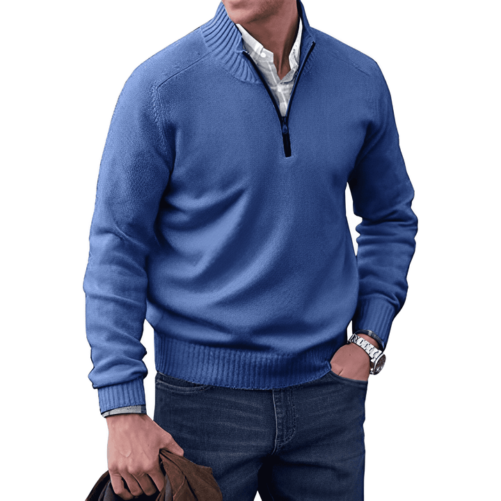 Mann in blauem Pullover mit Reißverschluss, weißem Hemd, Jeans, hält braune Jacke, modisch, elegant.