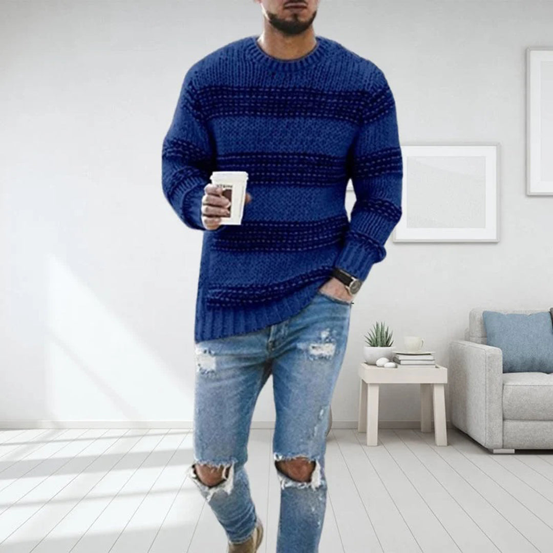 Mann in blauem Strickpullover mit Kaffeetasse, zerrissene Jeans, modernes Wohnzimmer.