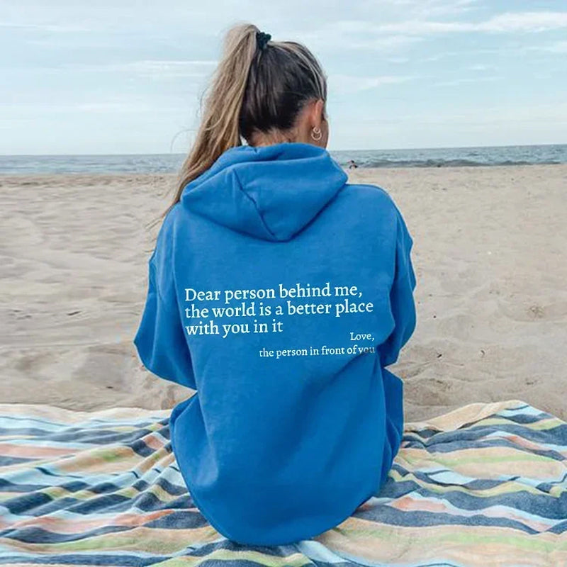 Frau im blauen Hoodie am Strand, Rückenansicht, mit motivierendem Zitat, Sand, Meer, Himmel.