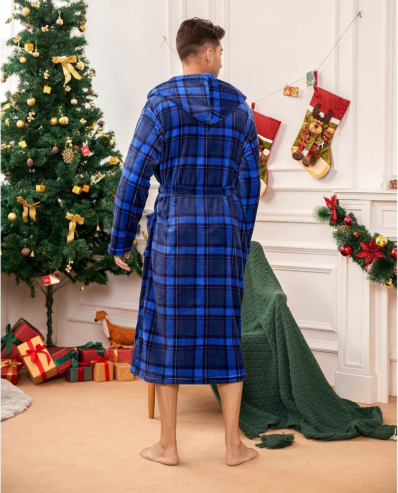 Mann im blauen karierten Bademantel vor Weihnachtsbaum und Geschenken im Wohnzimmer.