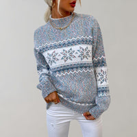 Frau in blauem Strickpullover mit Schneeflockenmuster, weiße Hose, modischer Winterlook.