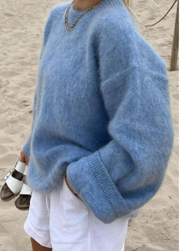 Frau in blauem, oversized Strickpullover aus Wolle am Strand, kombiniert mit weißen Shorts.