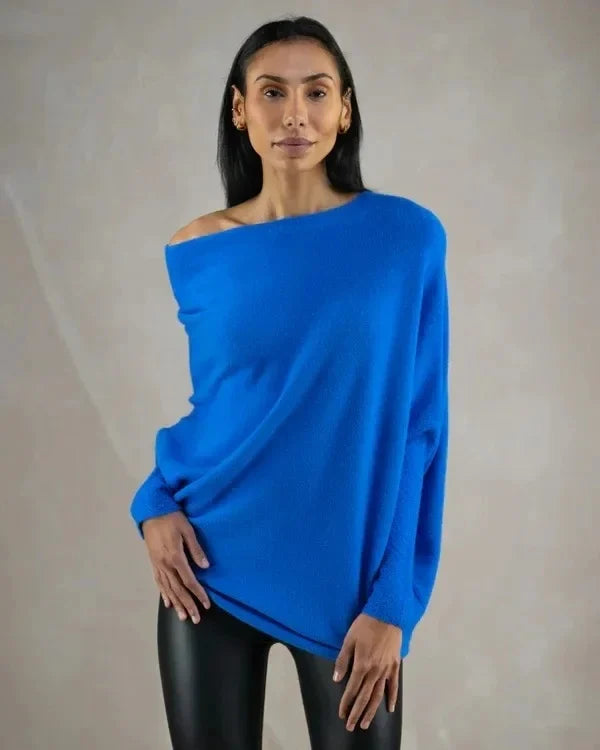 Frau in blauem Oversize-Pullover und schwarzen Lederleggings vor neutralem Hintergrund.