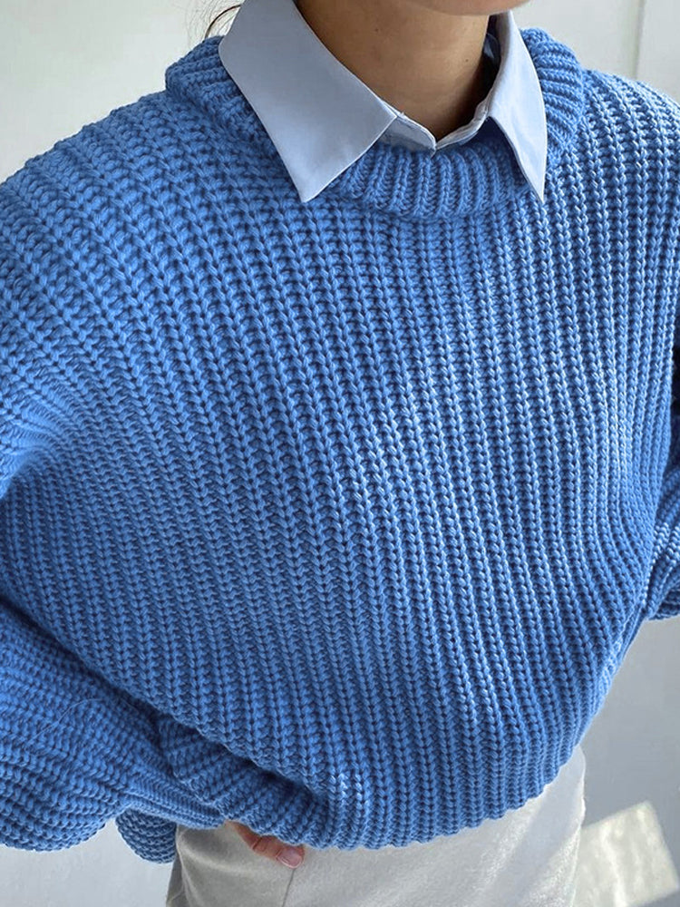 Frau in blauem Strickpullover mit Rundhalsausschnitt und weißem Hemd darunter.