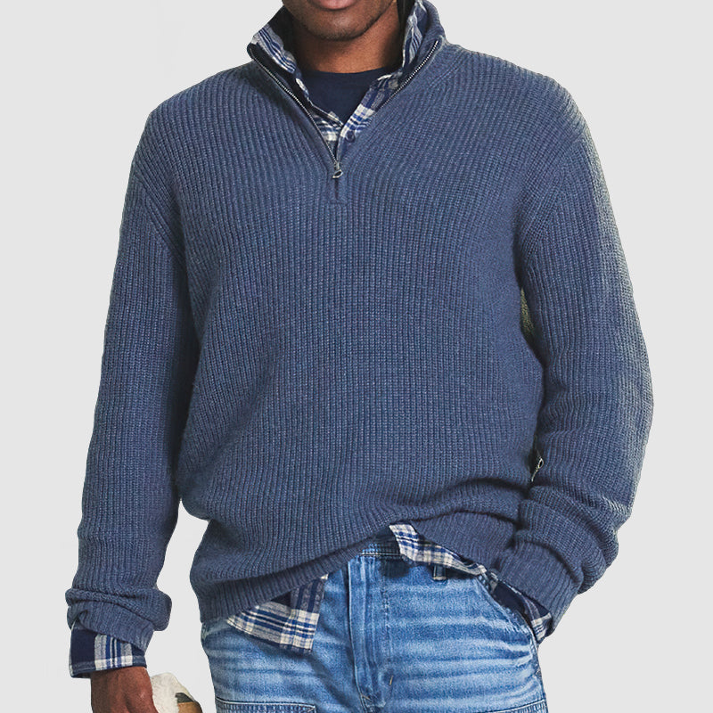 Mann in blauem Strickpullover mit Reißverschluss, kariertem Hemd und Jeans.