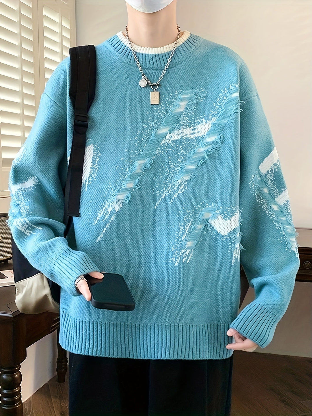 Person in blauem Strickpullover mit abstraktem Muster, hält Smartphone, modisch, lässig.
