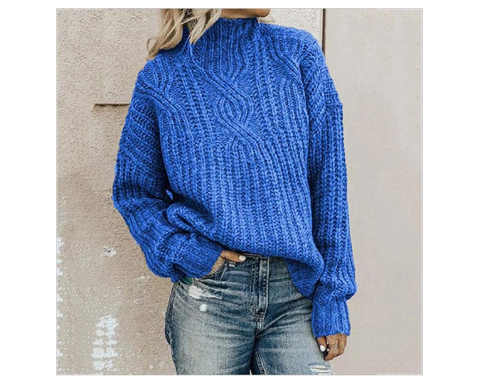 Frau in blauem Strickpullover und Jeans vor beiger Wand.