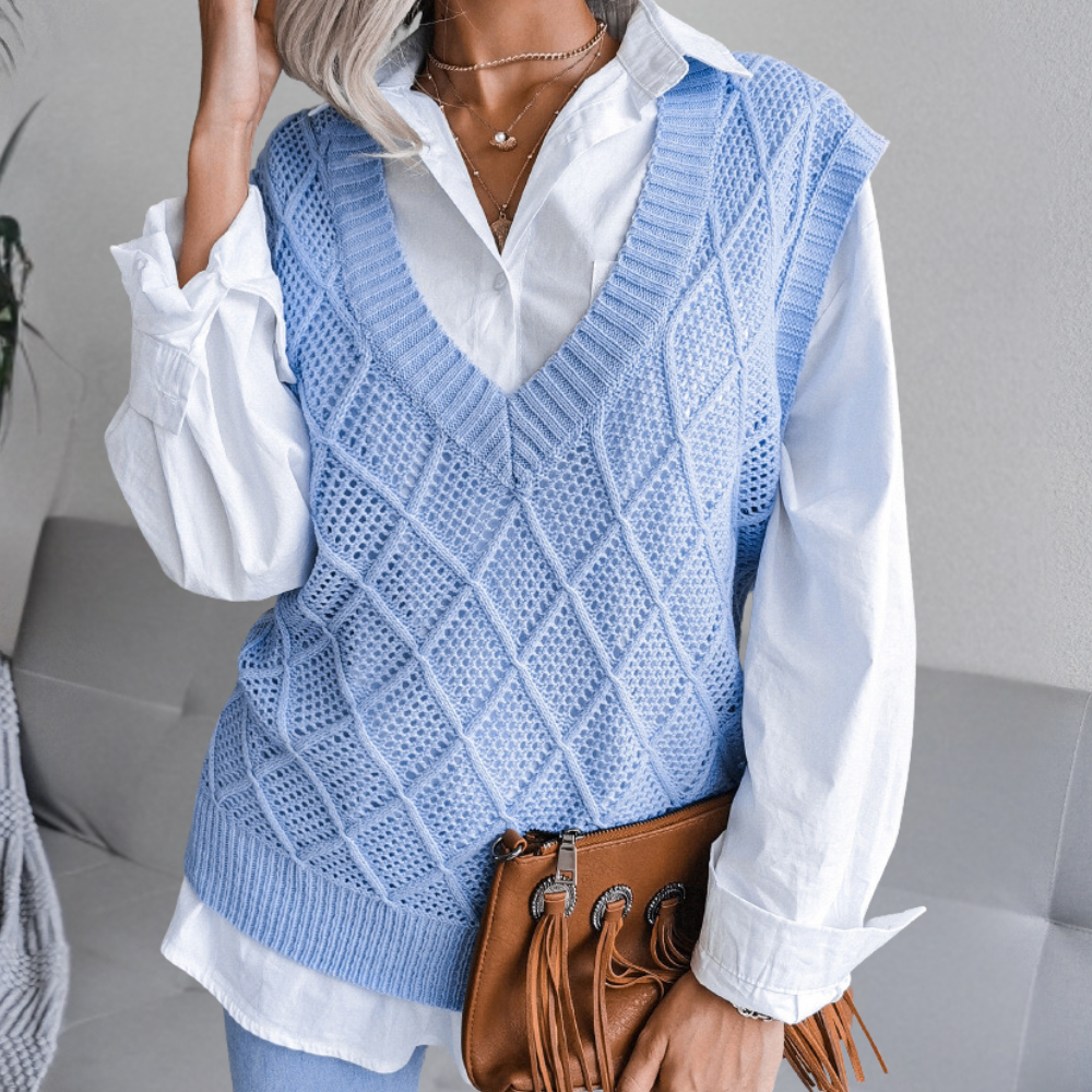 Frau in blauem Strickpullover und weißer Bluse, hält braune Fransenhandtasche.