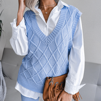 Frau in blauem Strickpullover und weißer Bluse, hält braune Fransenhandtasche.