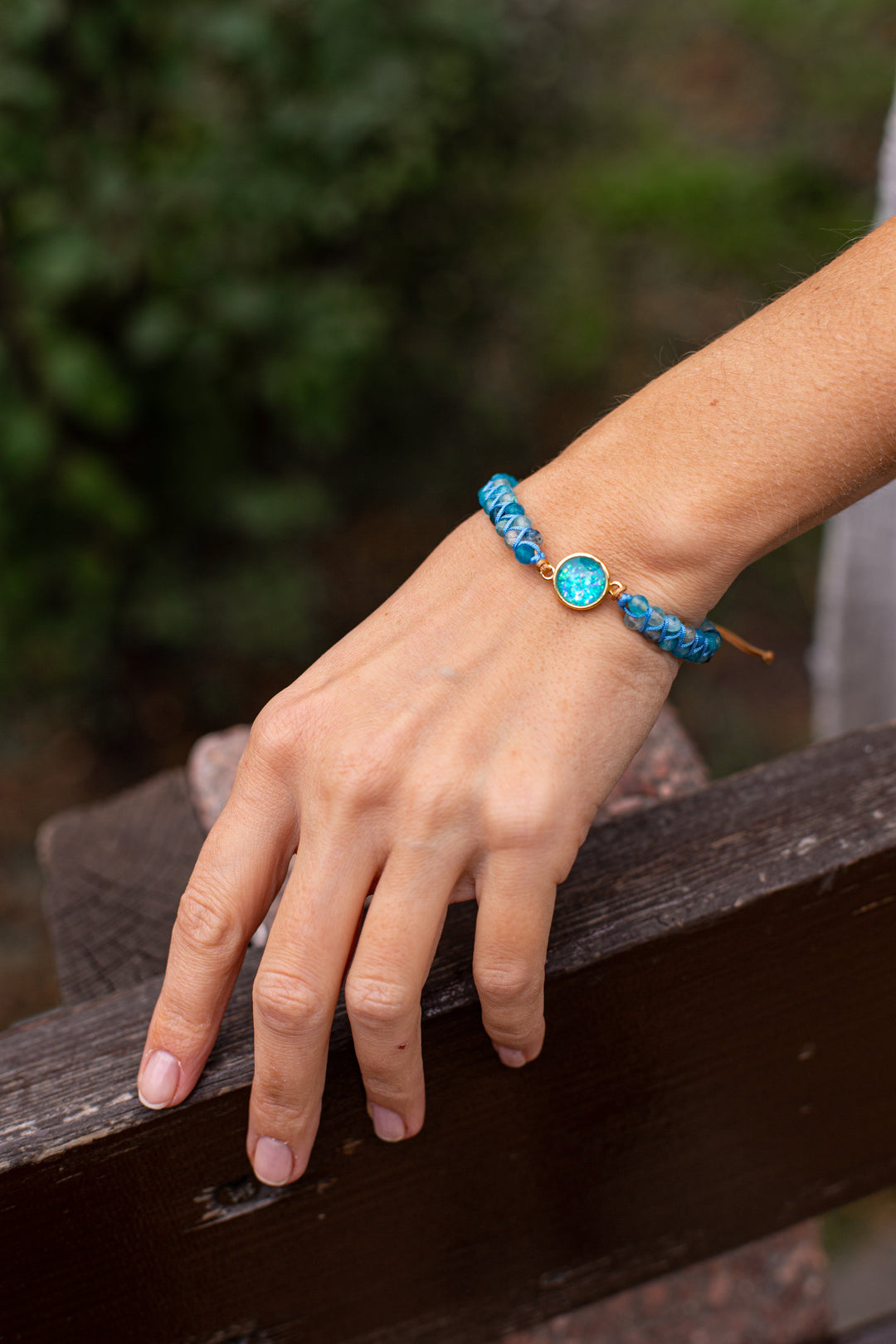 Hand mit blauem Armband aus Perlen und Kristall auf Holzbank, Schmuck, Modeaccessoire.