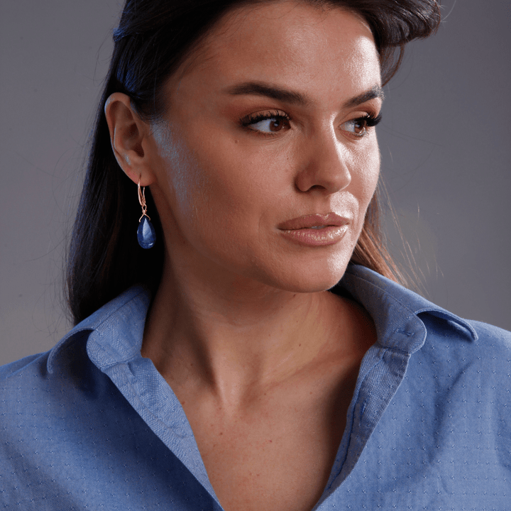 Frau mit blauer Bluse und blauen Ohrringen, elegantes Schmuckdesign, Modeaccessoire.