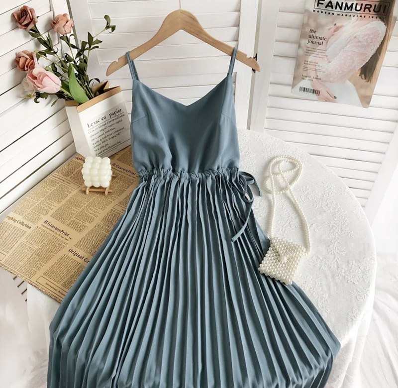 Blaues, plissiertes Sommerkleid auf Tisch mit Perlenhandtasche und Rosenstrauß.