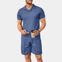 Mann in blauem Poloshirt und Shorts, hält Kaffeebecher und Smartphone.