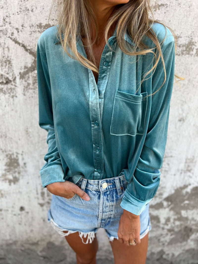 Frau in türkisfarbener Bluse und Jeansshorts vor Betonwand.