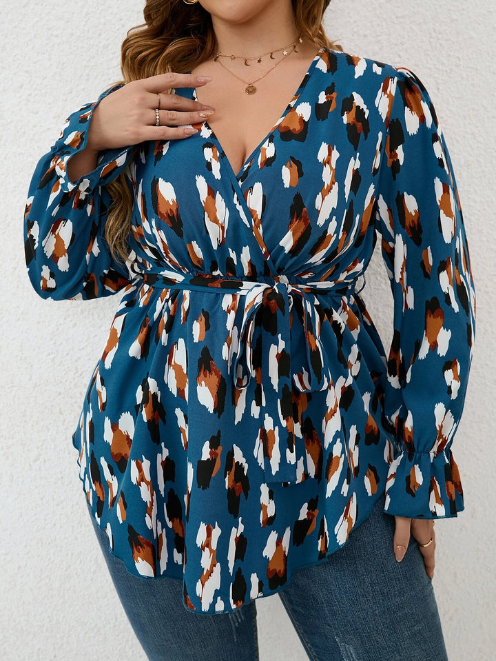 Frau in blauer, gemusterter Bluse mit V-Ausschnitt und Bindegürtel, modisch, elegant.