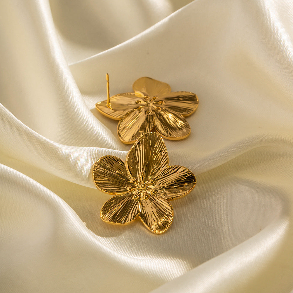 Goldene Blumen-Ohrringe auf cremefarbenem Satin, eleganter Schmuck, modische Accessoires.
