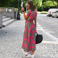Frau in pink-grünem Blumenkleid auf Kopfsteinpflasterstraße, trägt schwarze Tasche, Sonnenbrille.