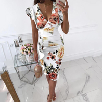 Frau in weißem Blumenkleid mit V-Ausschnitt, hält eine kleine Tasche, steht in modernem Raum.