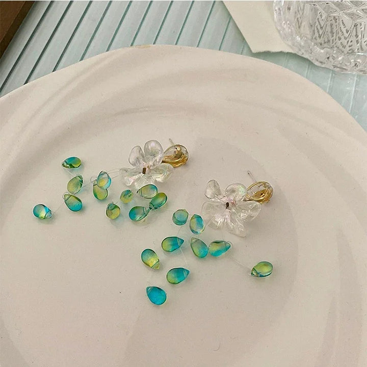 Blumenohrringe aus klarem Harz mit blauen und grünen Akzenten auf weißem Teller.