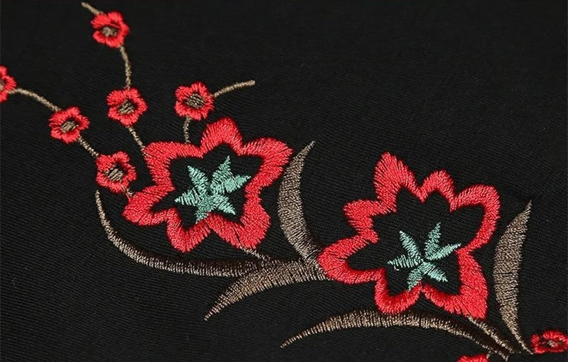 Schwarzer Stoff mit roter und grüner Blumenstickerei, elegantes Design, hochwertige Textilien.