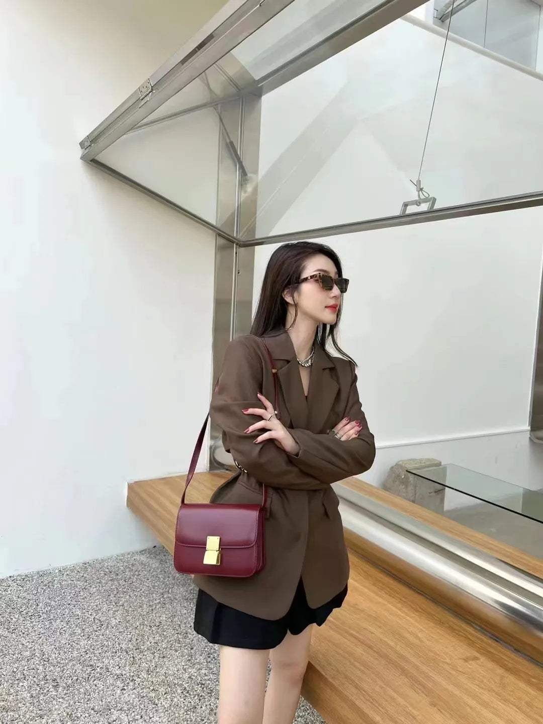 Frau mit braunem Blazer und roter Umhängetasche, moderne Architektur im Hintergrund.