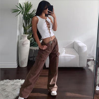 Frau in brauner Cargohose und weißem Top posiert in modernem Wohnzimmer.