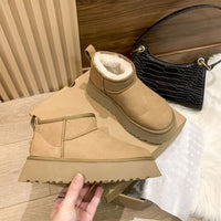 Braune Damen-Winterstiefel aus Wildleder mit Fellfutter auf Holzboden, neben schwarzer Handtasche.