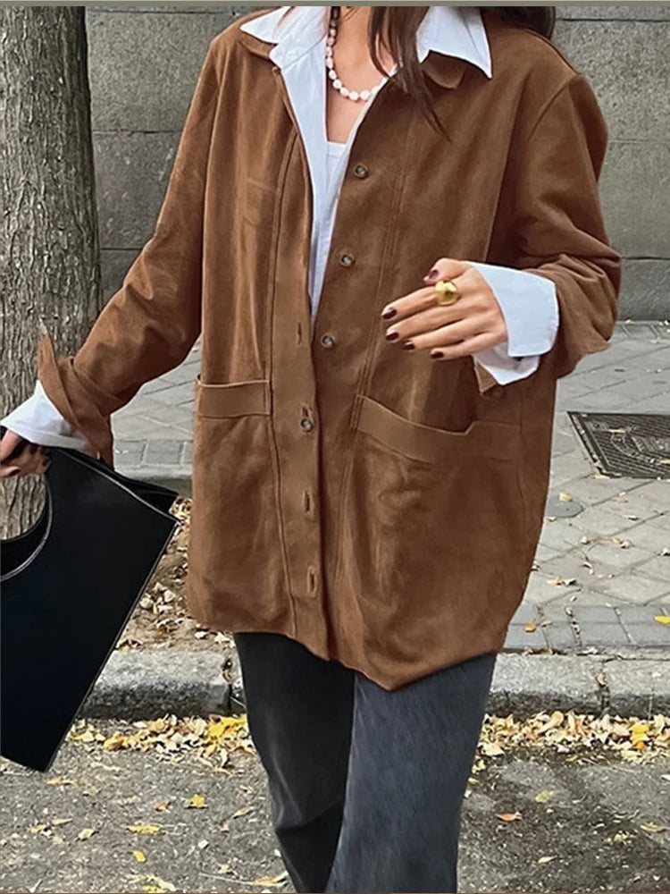 Frau in brauner Wildlederjacke mit weißen Manschetten, schwarze Tasche, Herbstmode.