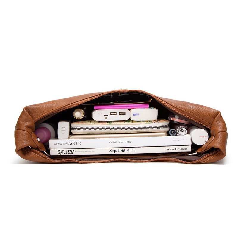 Braune Ledertasche mit Zeitschriften, Powerbank und Kosmetikartikeln, ideal für Reisen.