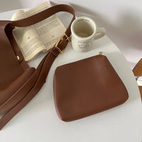 Braune Ledertasche mit passender Geldbörse und Kaffeetasse auf weißem Tisch.