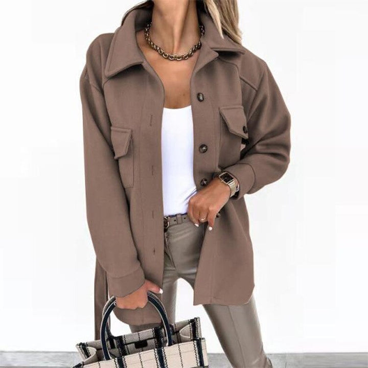 Frau in brauner Jacke, weiße Bluse, Lederhose, hält karierte Tasche, modisch, elegant.