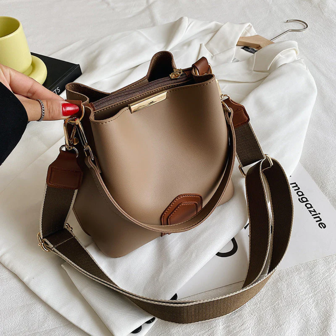 Damenhandtasche aus braunem Leder mit verstellbarem Schultergurt auf weißem Hemd.