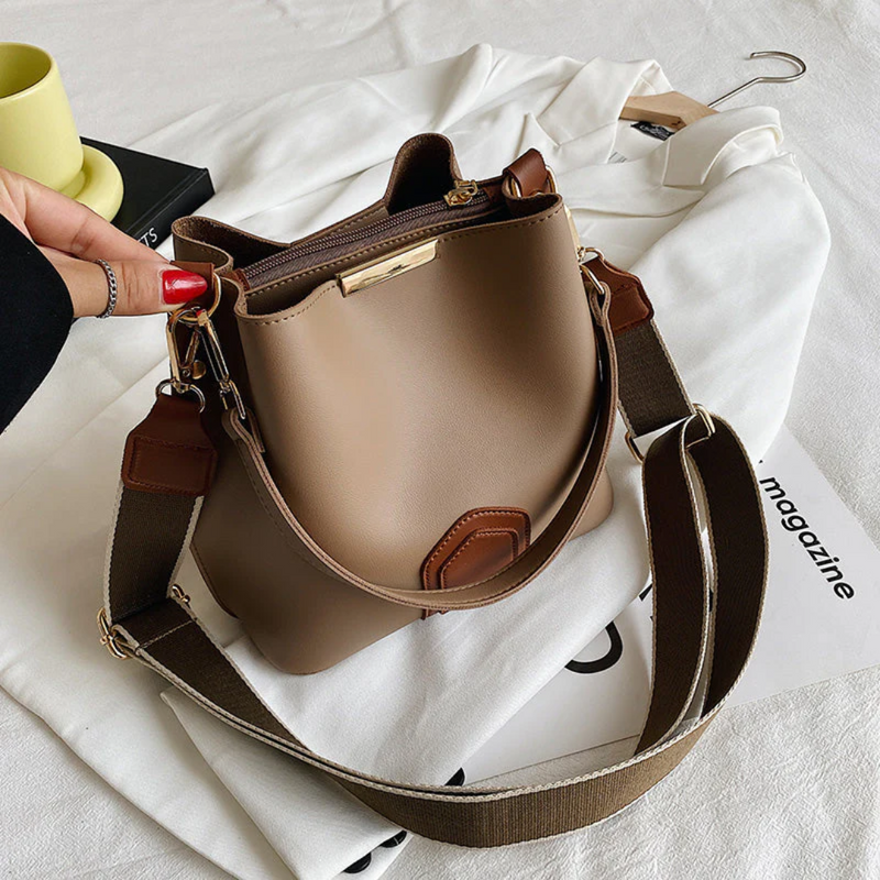 Damenhandtasche aus braunem Leder mit verstellbarem Schultergurt auf weißem Hemd.