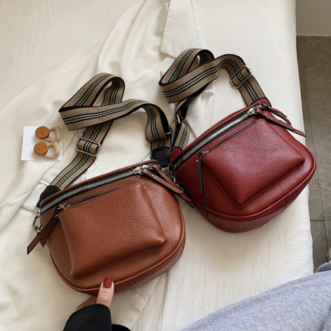 Zwei braune Leder-Umhängetaschen mit gestreiften Trägern auf weißem Hintergrund.