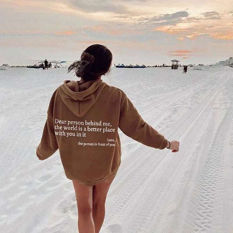 Frau am Strand in braunem Hoodie mit Spruch, Sonnenuntergang, Sand, Freizeitkleidung.