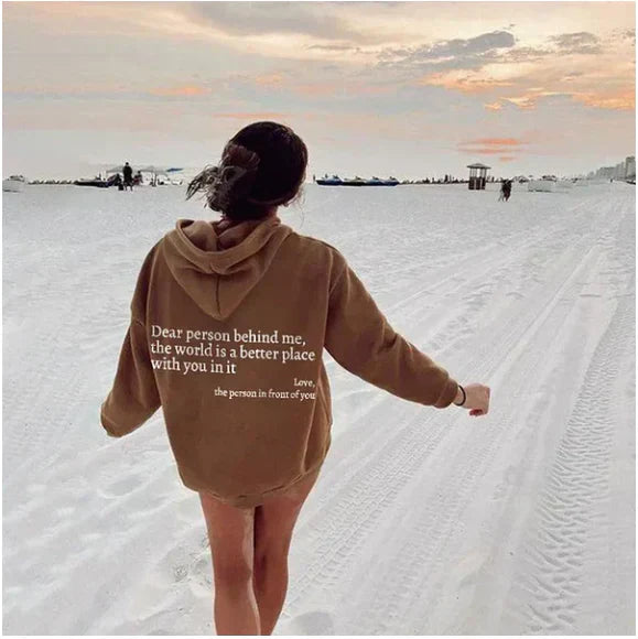 Frau in braunem Hoodie am Strand bei Sonnenuntergang, Rückenansicht, inspirierender Text.